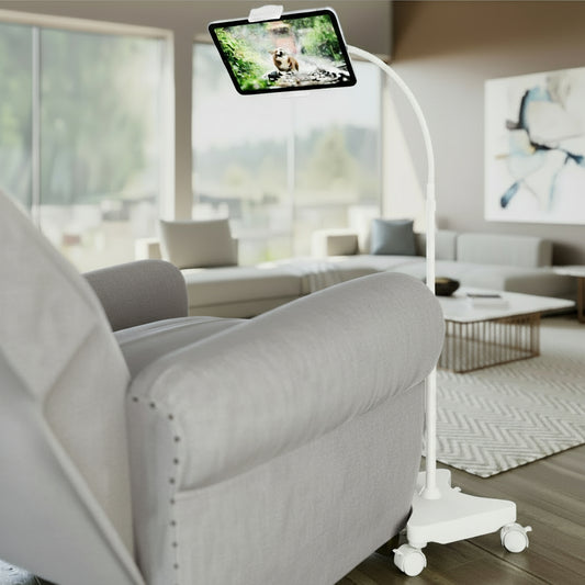 A black gooseneck tablet floor stand with casters, positioned next to a chair, displaying a tablet screen.